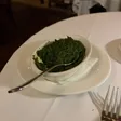 A bowl of creamed spinach on a white plate with a serving spoon.