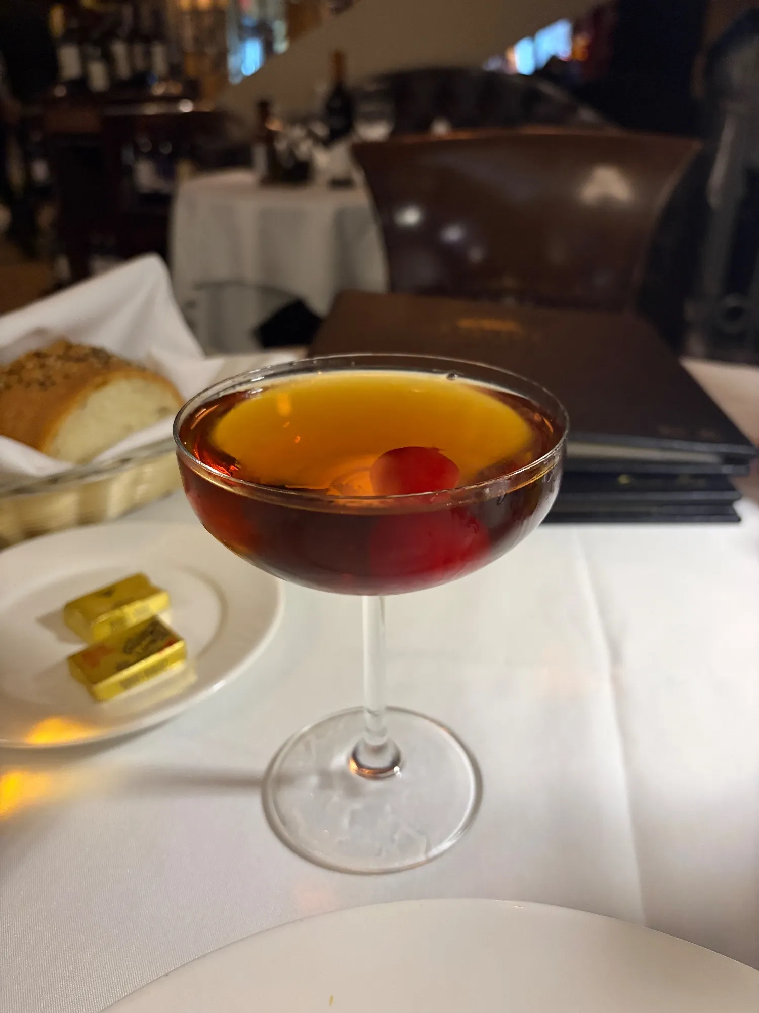 A Manhattan in a stemmed coupe with a red cherry submerged in the drink.