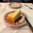 A slice of cheesecake on a red-patterned plate with a raspberry and a stripe of red sauce.