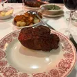 A seared filet on a red-patterned plate, with a side of hash browns and wine glasses behind.