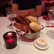 A metal basket containing pretzel bread and rolls beside a covered butter dish.