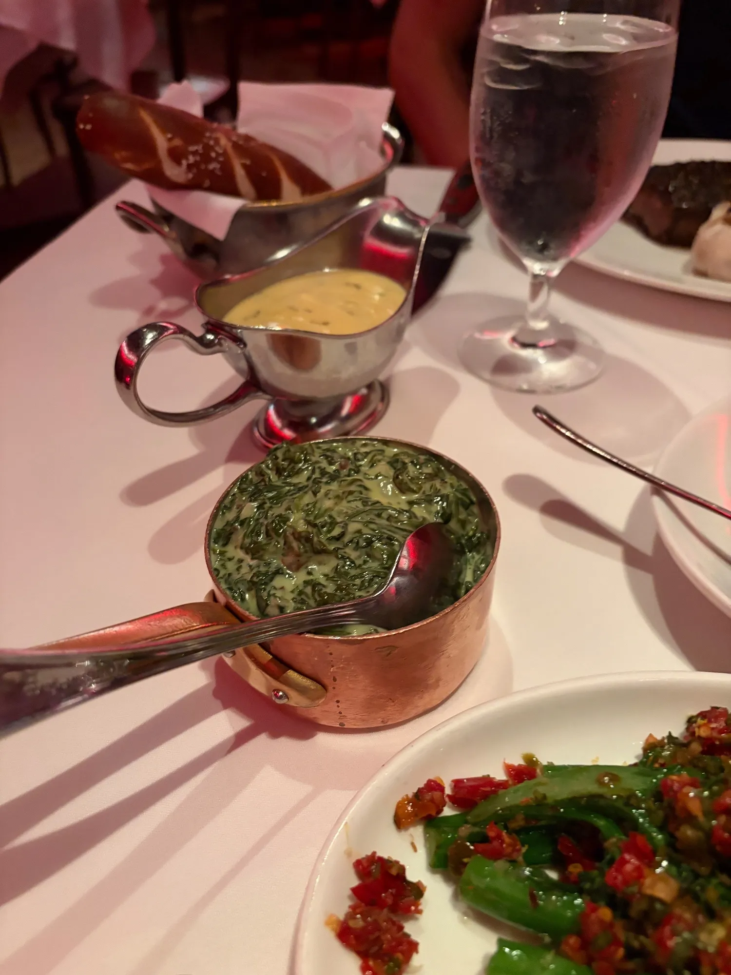 Creamed spinach in a copper pan with a serving spoon, surrounded by other dishes and sauce boats.