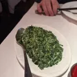 Oval white dish of creamed spinach with a serving spoon; a dish of red sauce at the lower right.