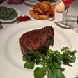 Round filet on a white plate with watercress, a side of fries, creamed spinach, red sauce and a stemmed drink in the background.